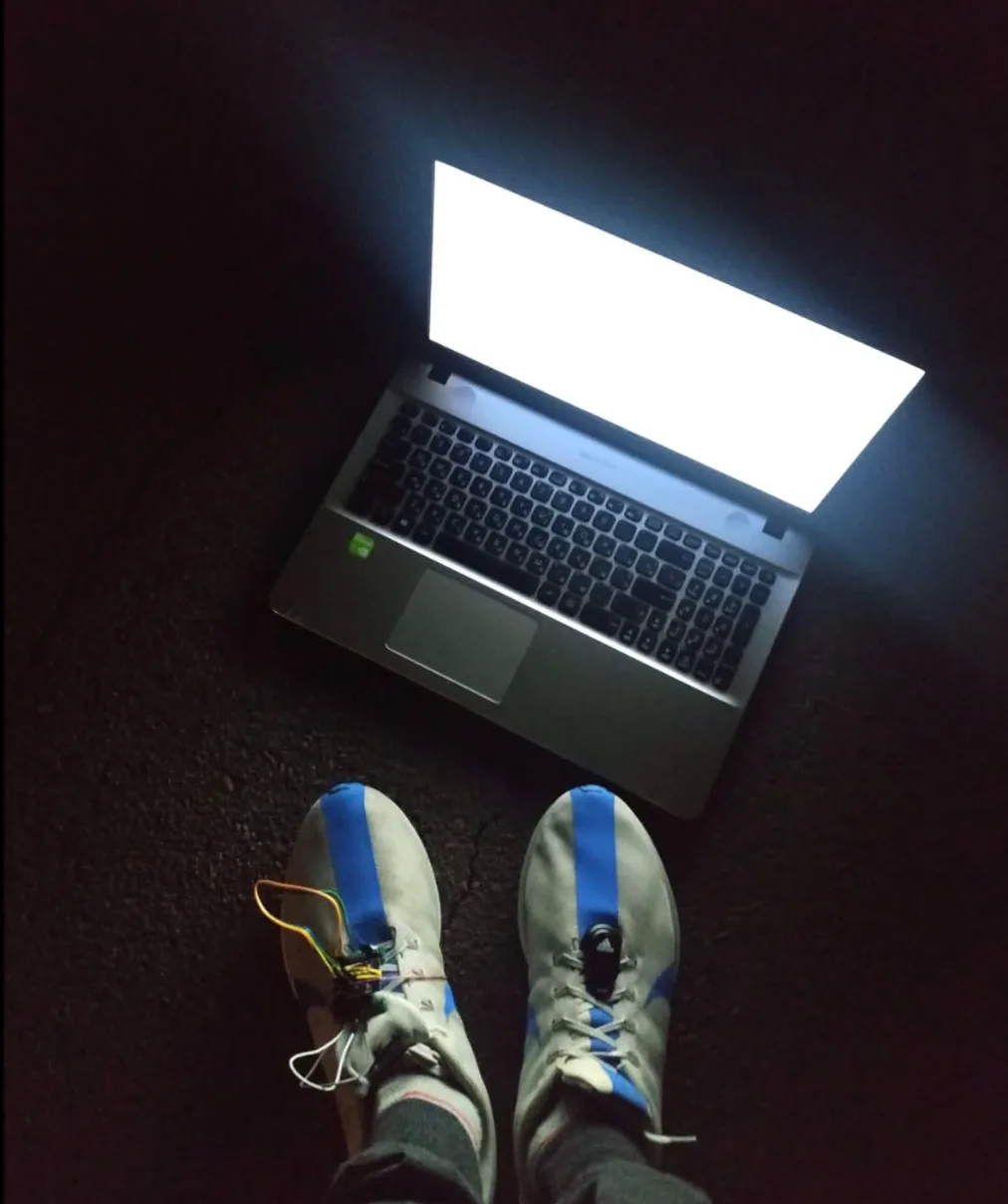 A laptop glowing on the ground in the dark, running shoes with the sensor zip-tied to the laces