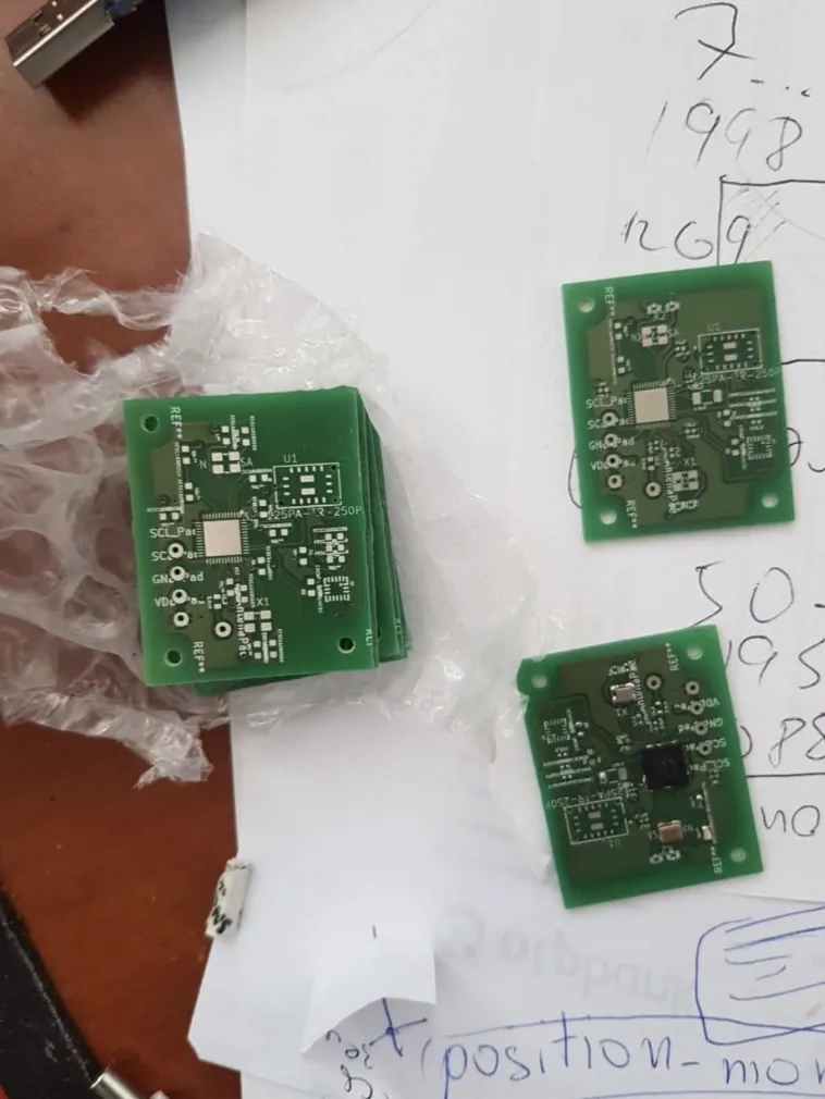 A stack of custom green printed circuit boards on bubble wrap next to handwritten notes
