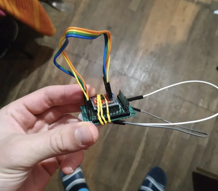 A hand holding the first prototype: a small dev board with ribbon cables and sensor tubing